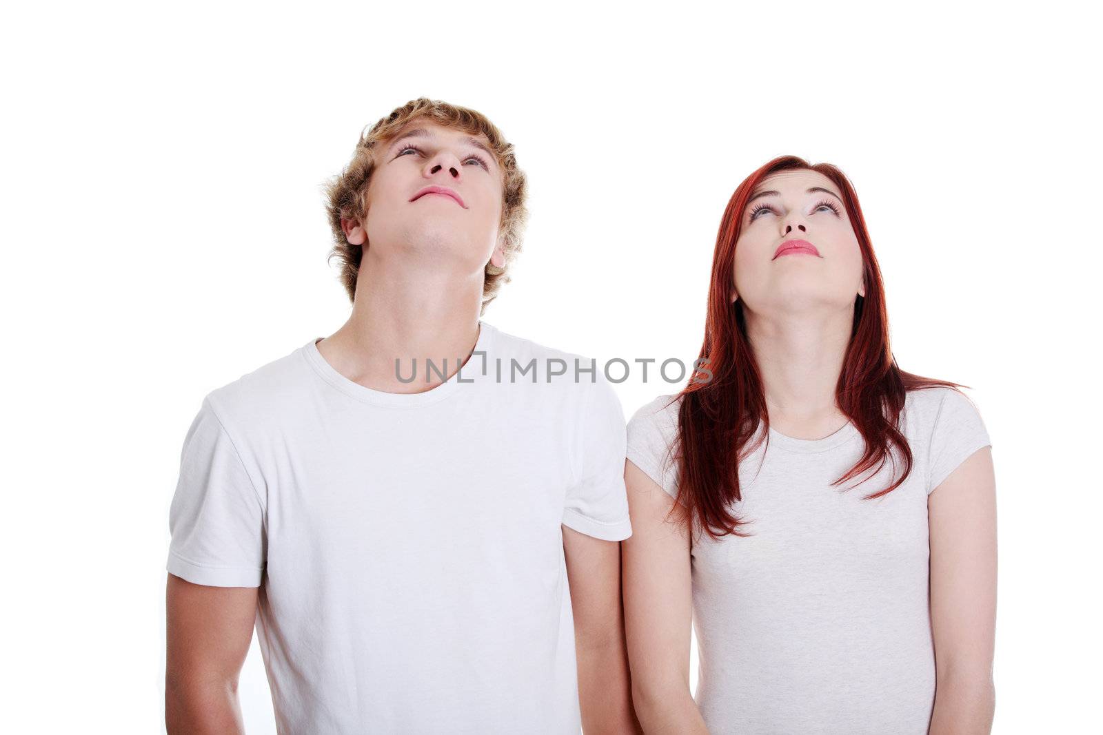 Young caucasian couple looking up against white background.