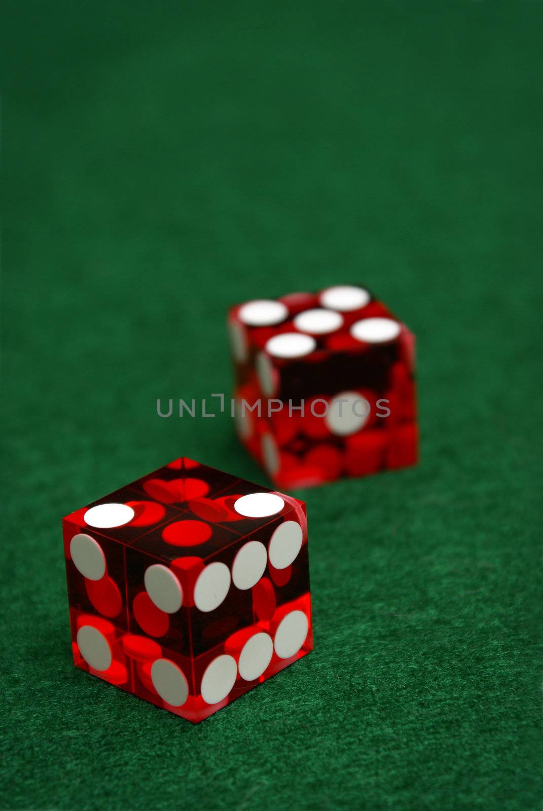 A pair of casino quality red dice lie on a green felt table with the number seven rolled.