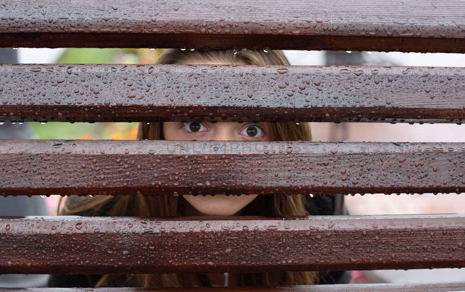 Teen girl looking through wet fence with water drops