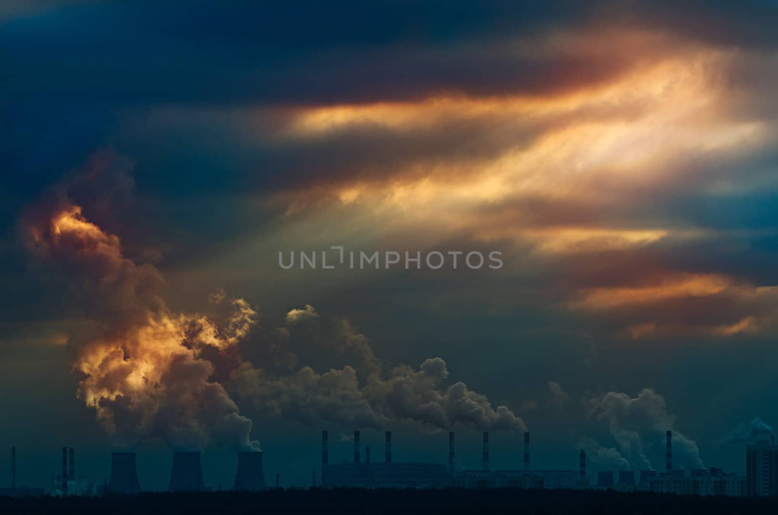 Rays of light emerging from moody cloudy sunset sky with plants and smoke in the background