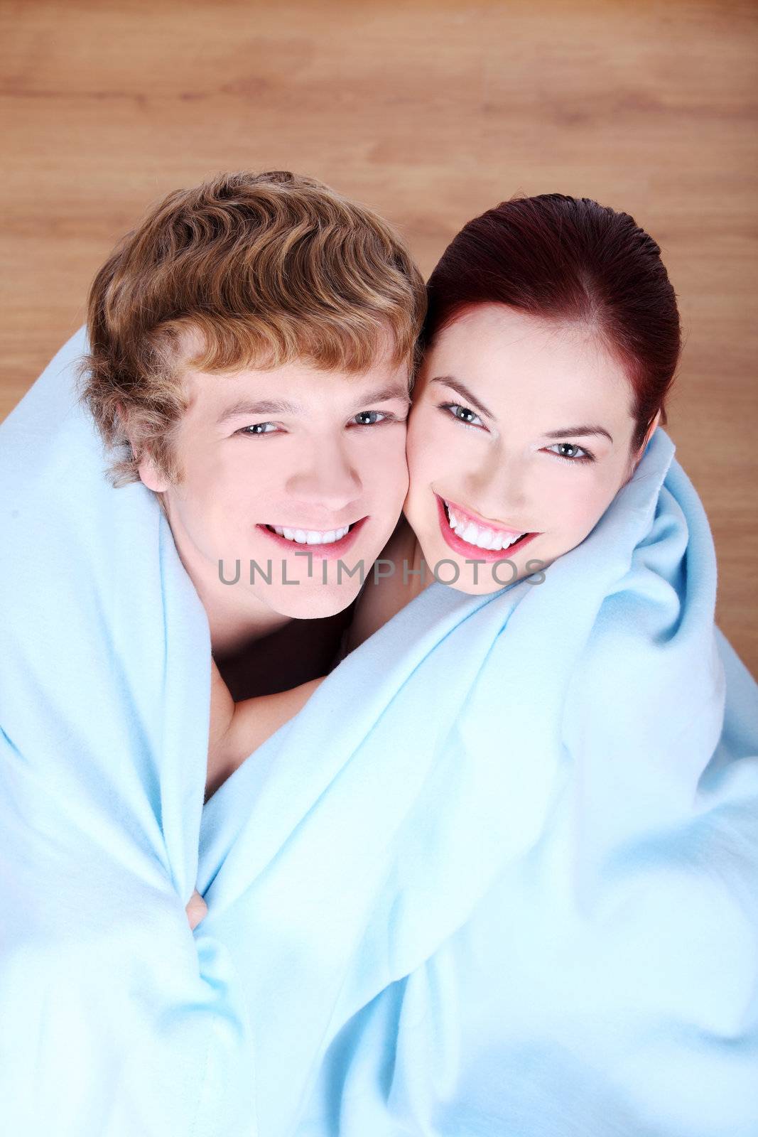 Young caucasian couple wrapped in blue blanket.