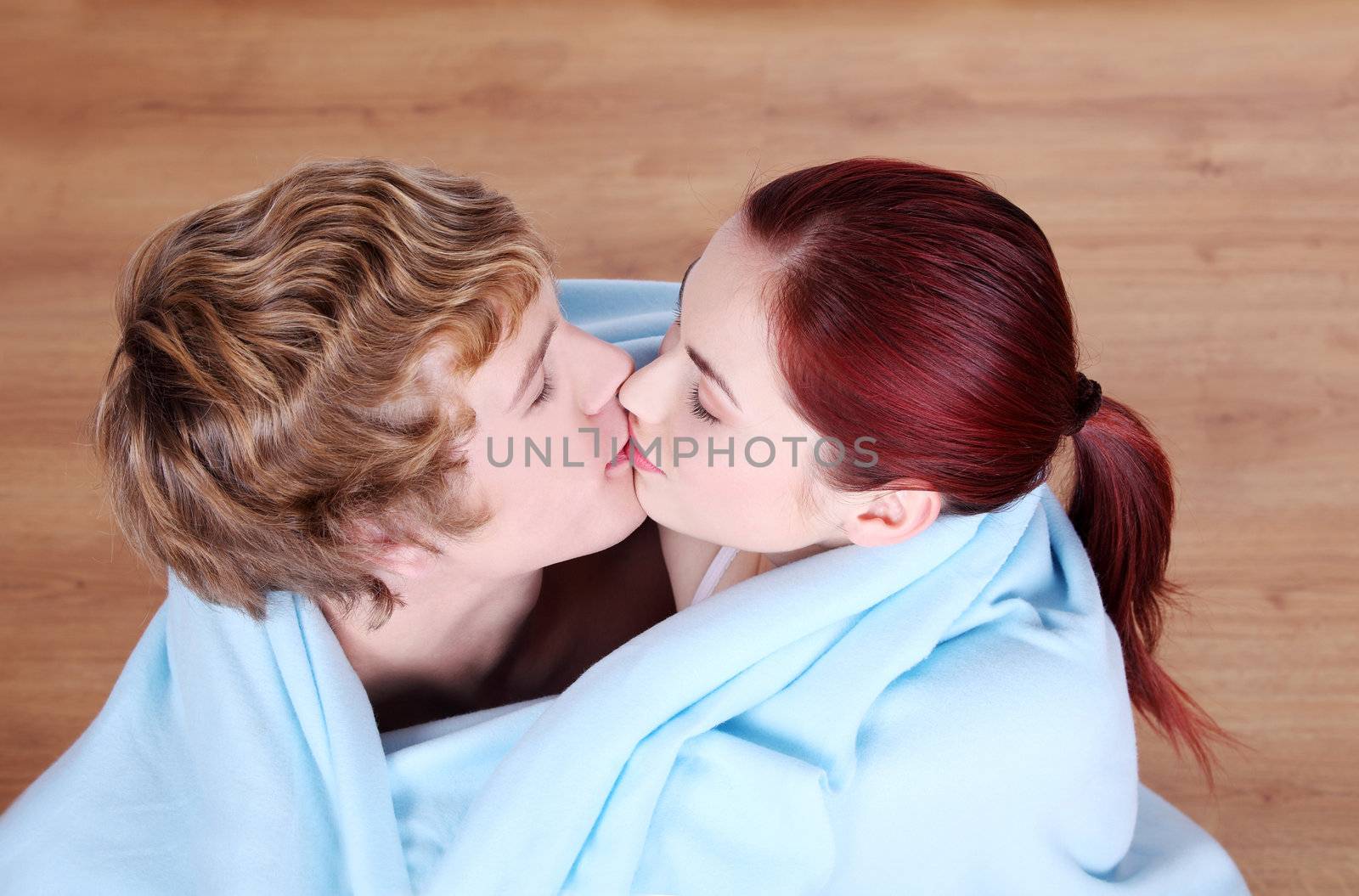 Young caucasian couple kissing wrapped in blue blanket.