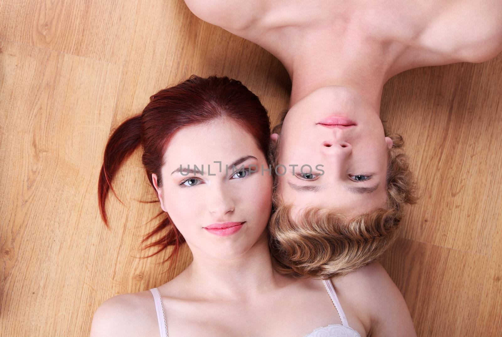 Happy young caucasian couple lying head to head on the floor.