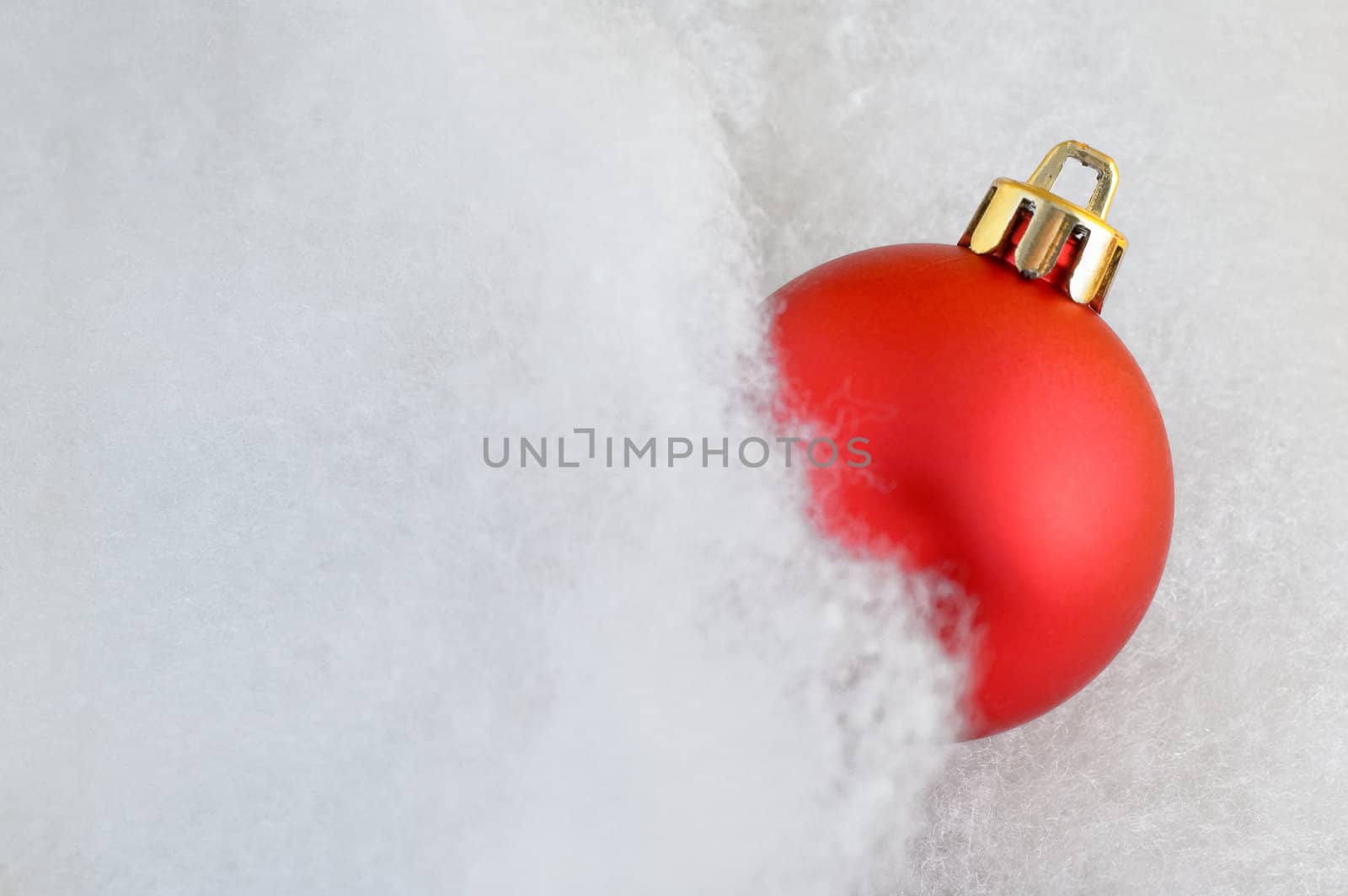 Close up of a red bauble in fluffy cotton with copy space and slight glow