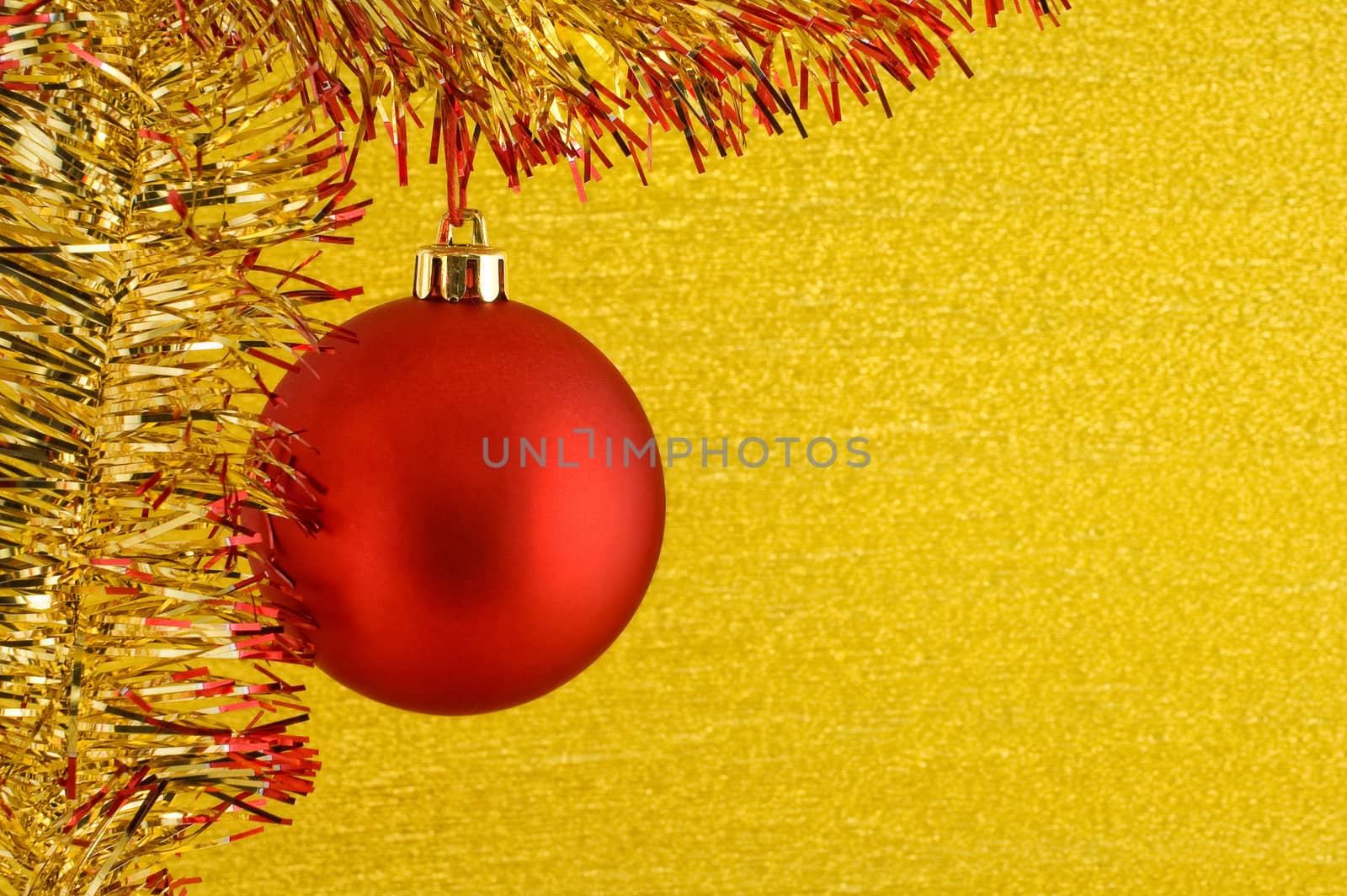 Red Christmas bauble hanging from glittering tinsel on golden background. Copy space for text.