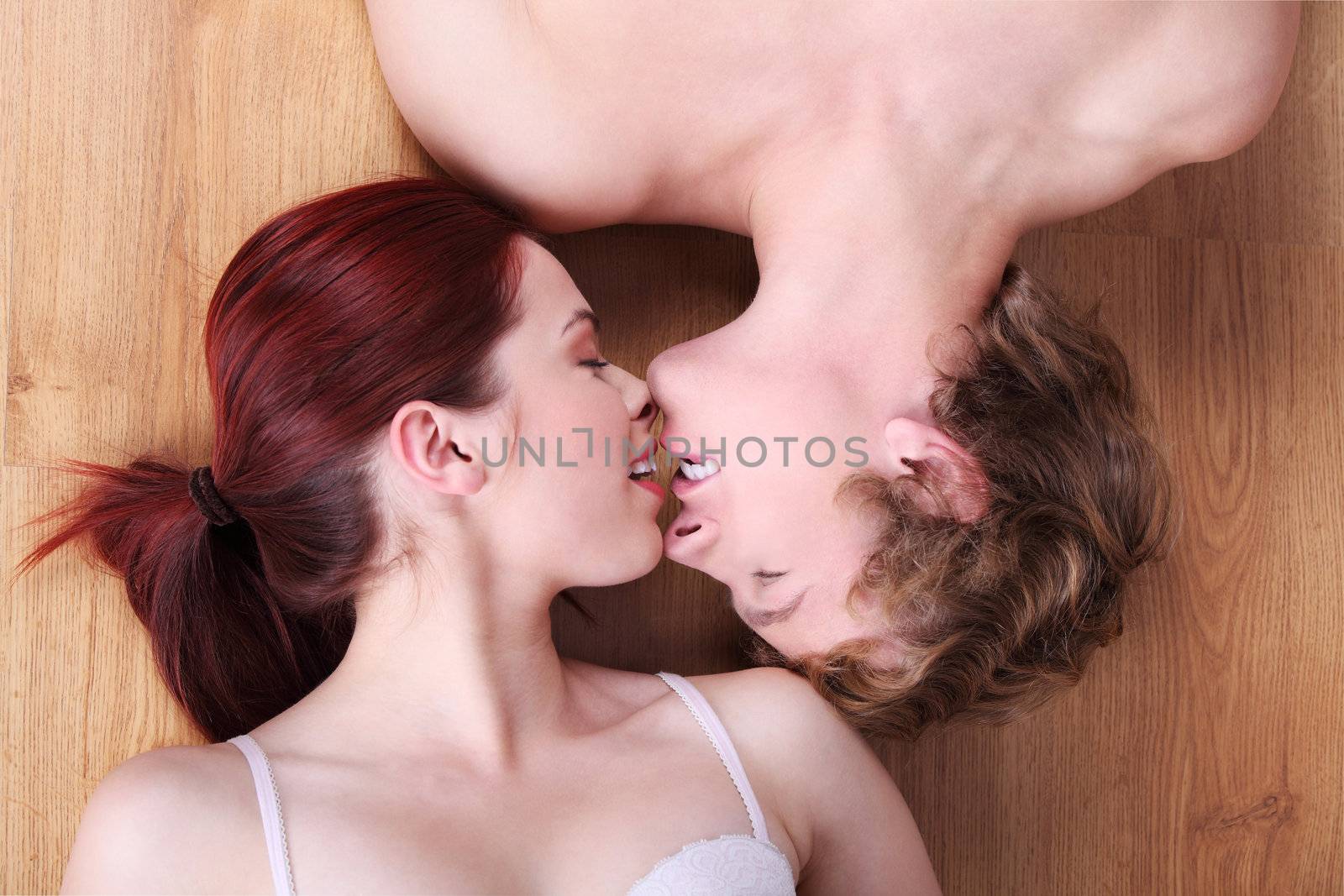 Young caucasian couple lying on the floor and kissing with their eyes closed.