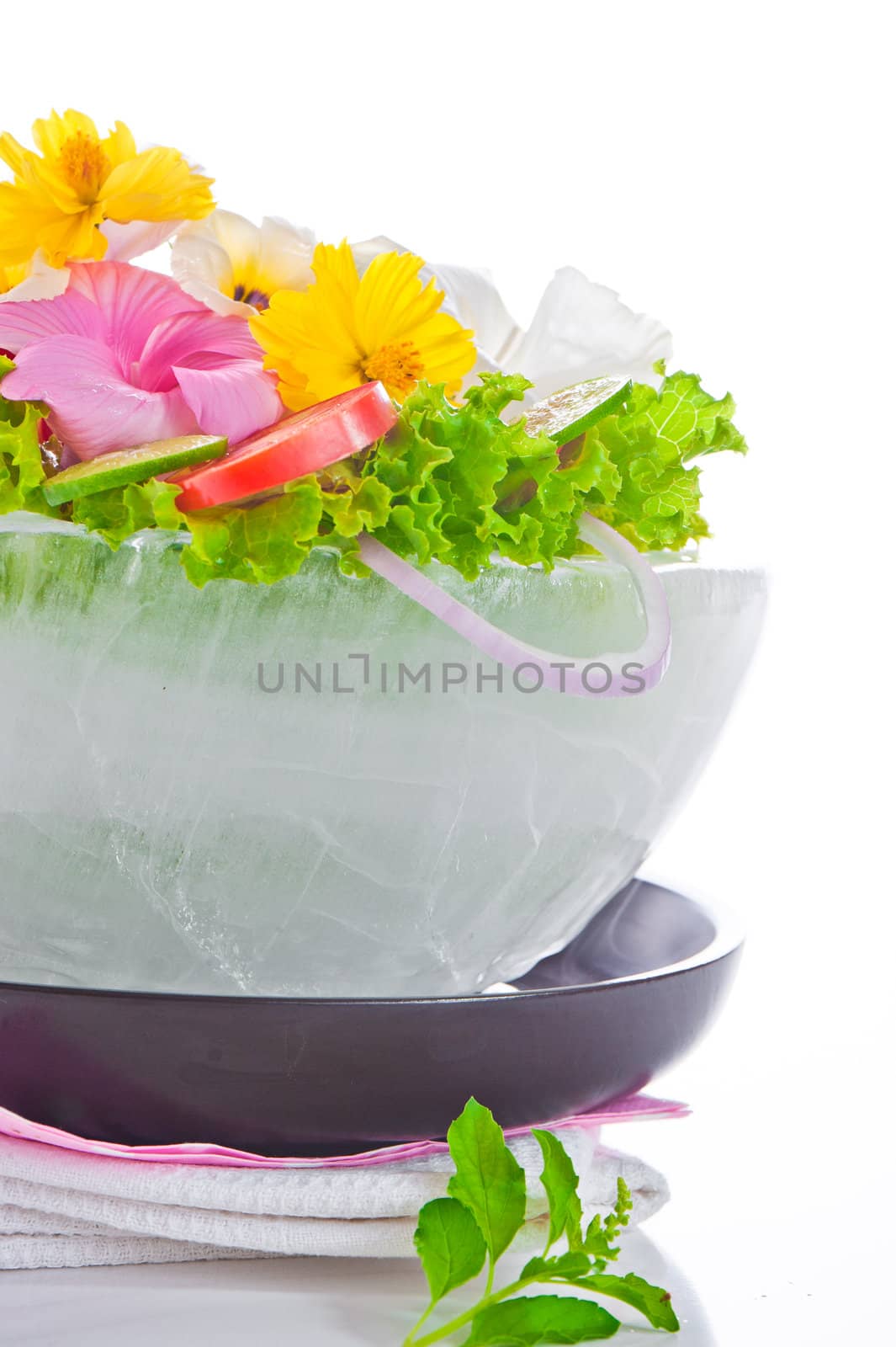 Green salad with tomatoes and various edible flowers in a bowl of ice on a white background