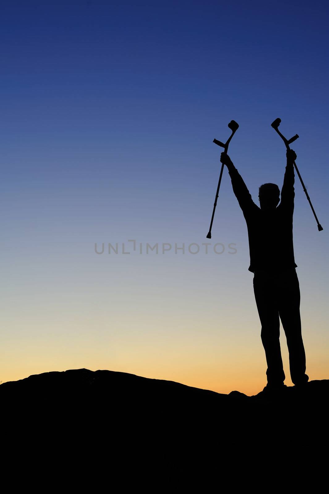 Silhouette of a man facing the dawn holding his crutches high above his head, greeting the sunrise. 