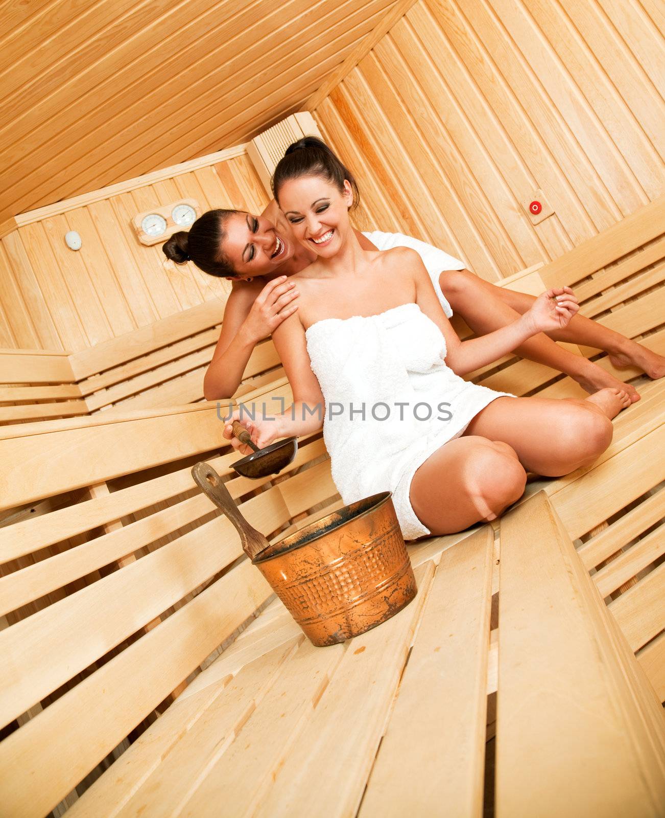 Two beautiful females having fun in sauna, hugging and laughing