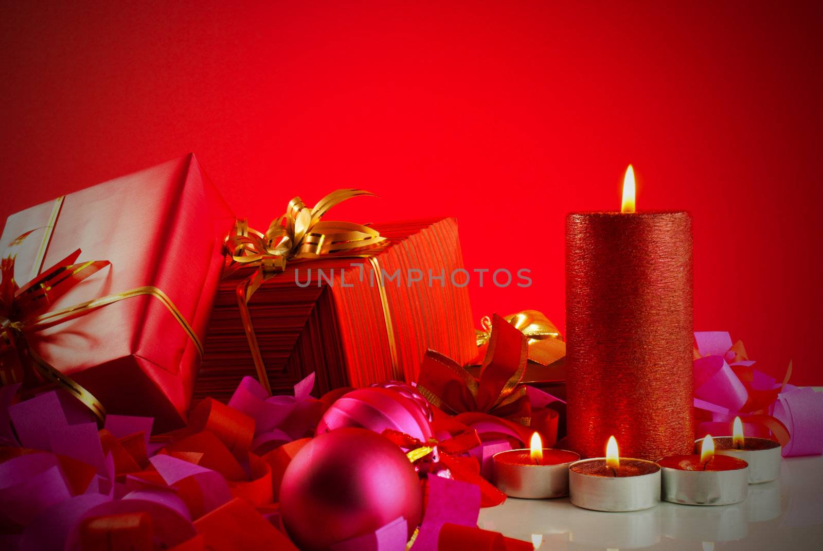 Christmas gifts and candles over red background