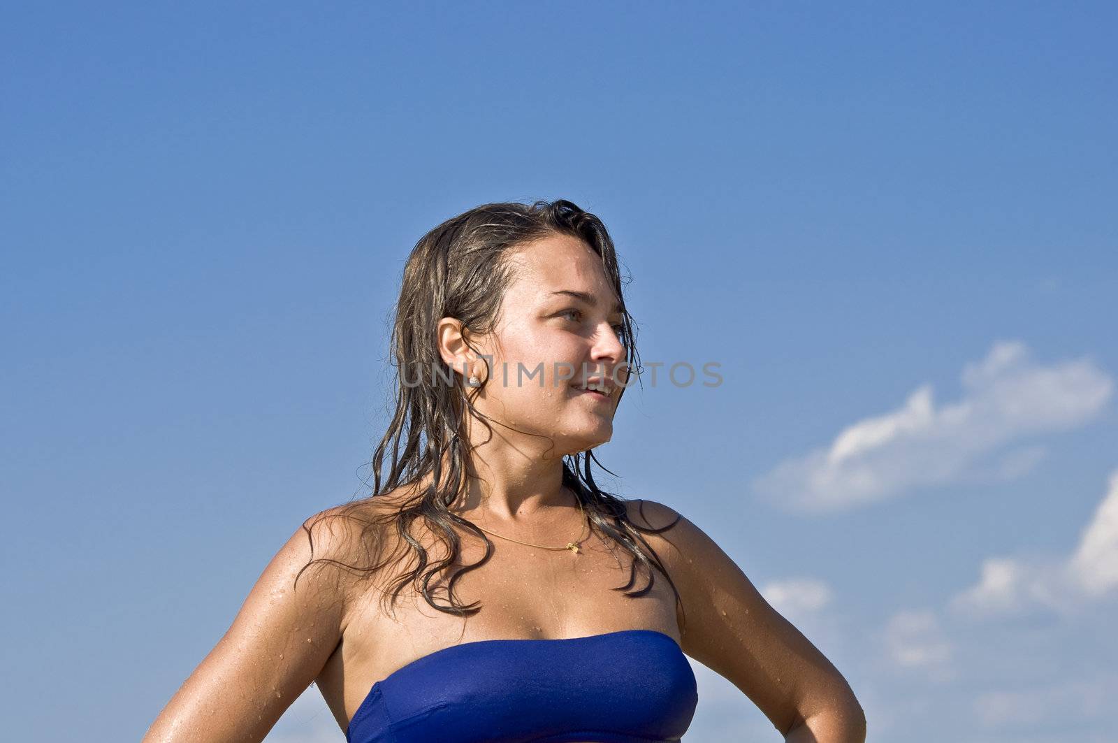 Close-up portrait of beautiful young cute woman in bikini smiling at the blue sky. Water droplets on the skin.