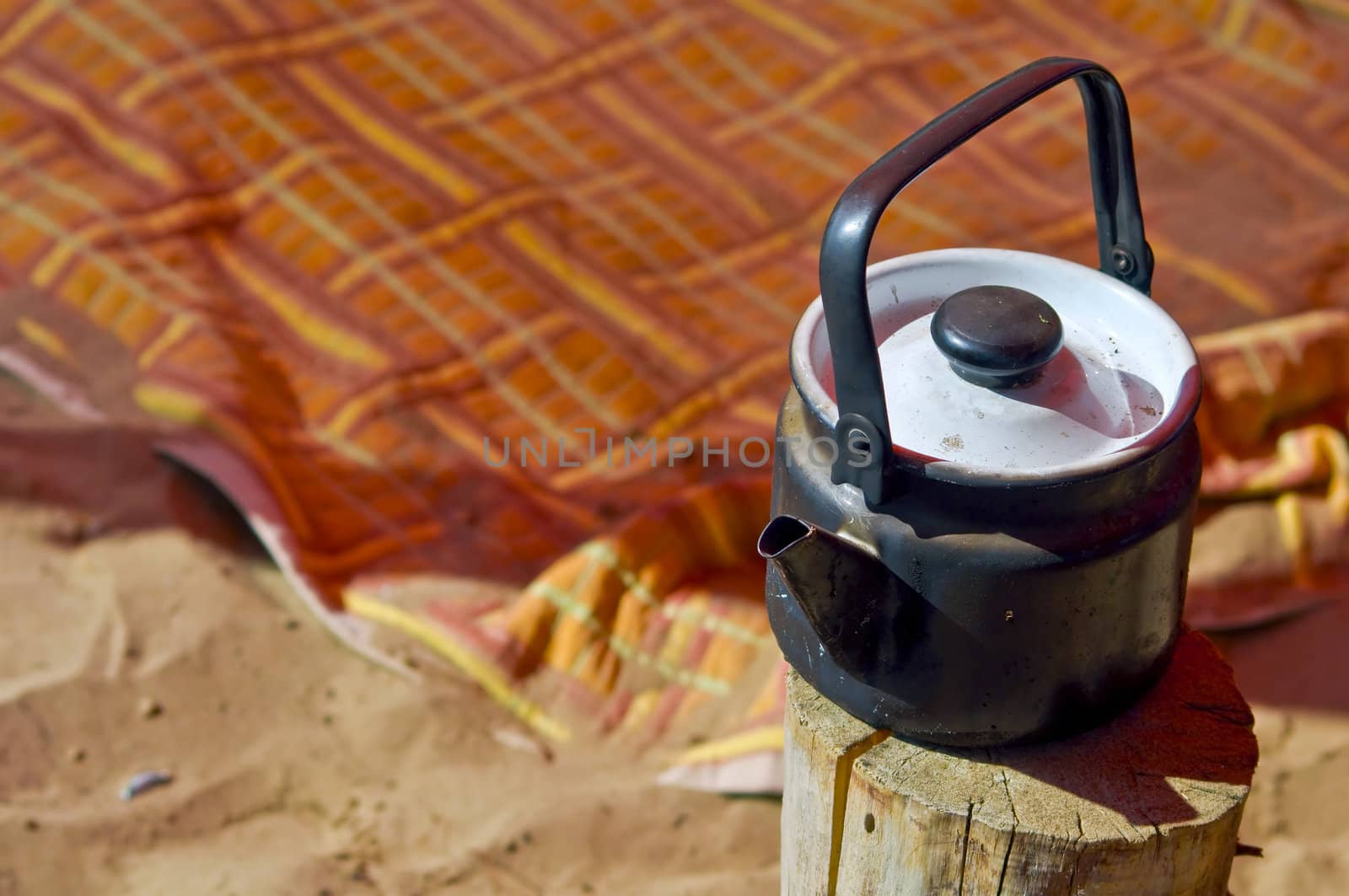 Sooty teapot is on the stump against the backdrop of colorful blankets on the beach. Summer, shallow depth of field.