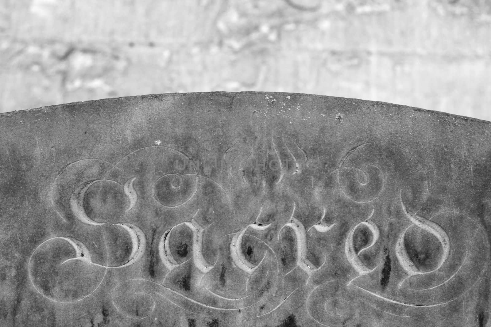 black and white image of a grave stone with the word "sacred" lot of stone texture visible