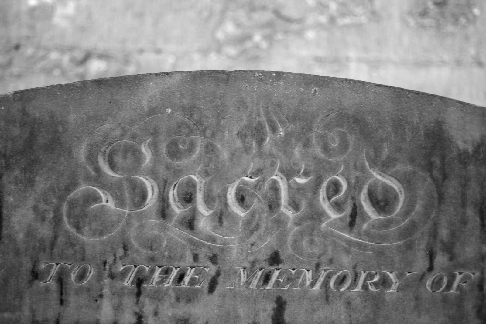 black and white image of a grave stone with the word "sacred to the memory of" lot of stone texture visible