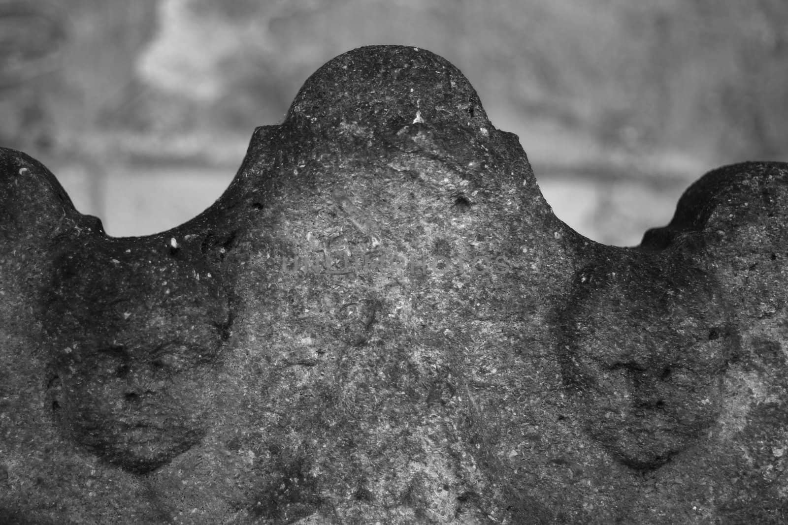 black and white image of a grave stone with the word "sacred to the memory of" lot of stone texture visible the deterioting heads of two old stone angels.