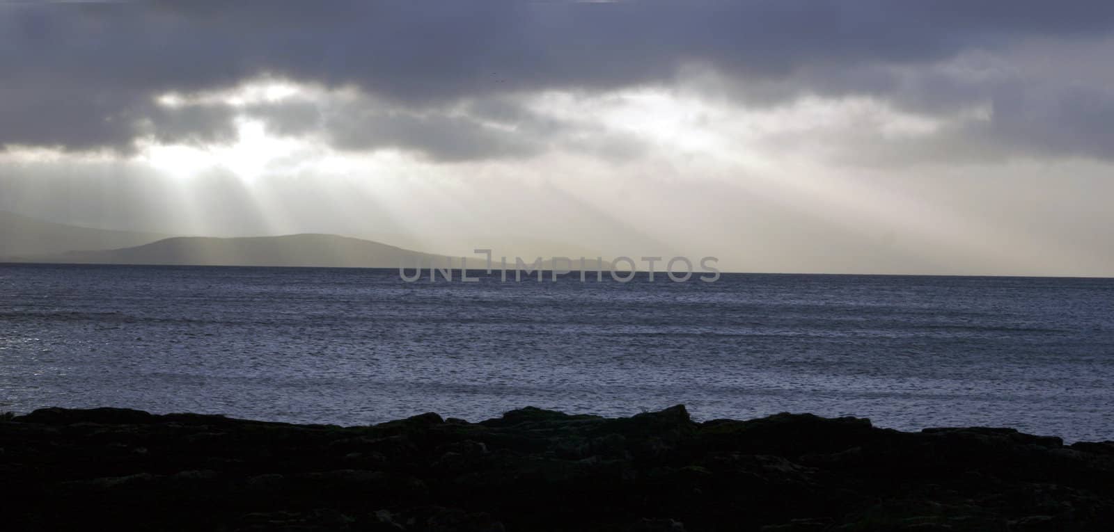 The scottish island of Arran at a stormy day, seen from the western coast of the mainland (Mull), sun rays or beams over the sea