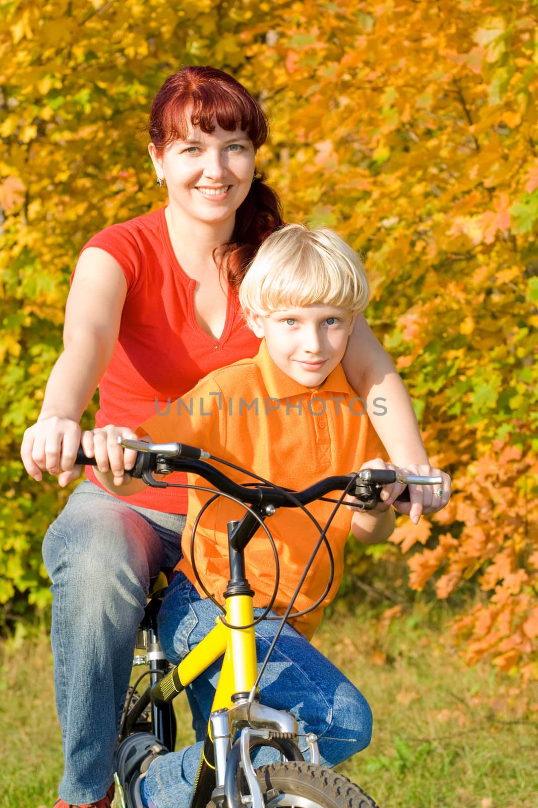 Young happy women and son on bicycle in the fall