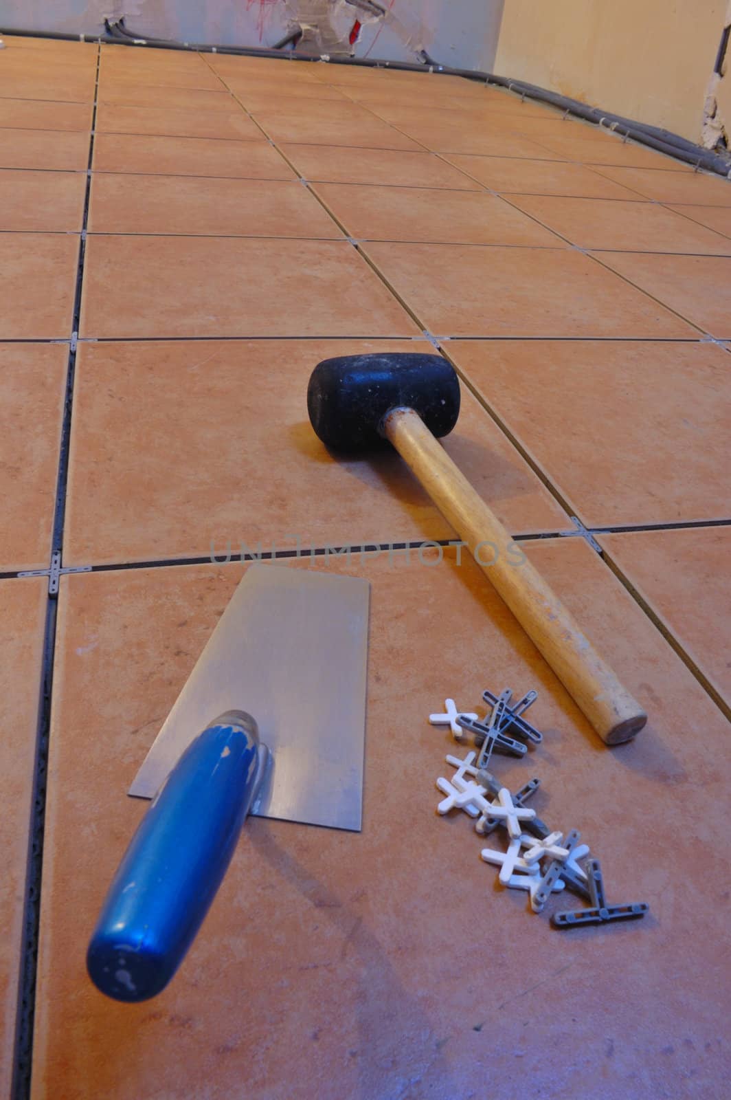 Close up of a workman's tools on a floor that is being tiled. More work in progress visible in background.