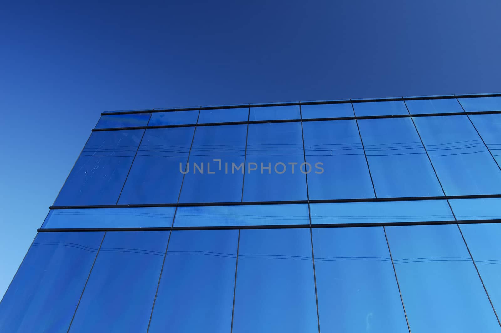 A modern office block with a glass facade reflects the clear blue of a cloudless sky, with some power lines.