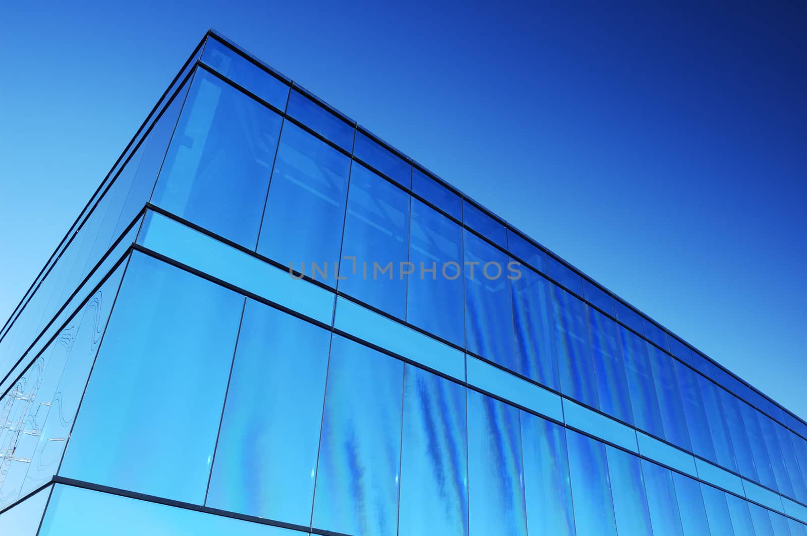 A modern office block with blue glass facade reflects a clear sky. Space for text in the sky.