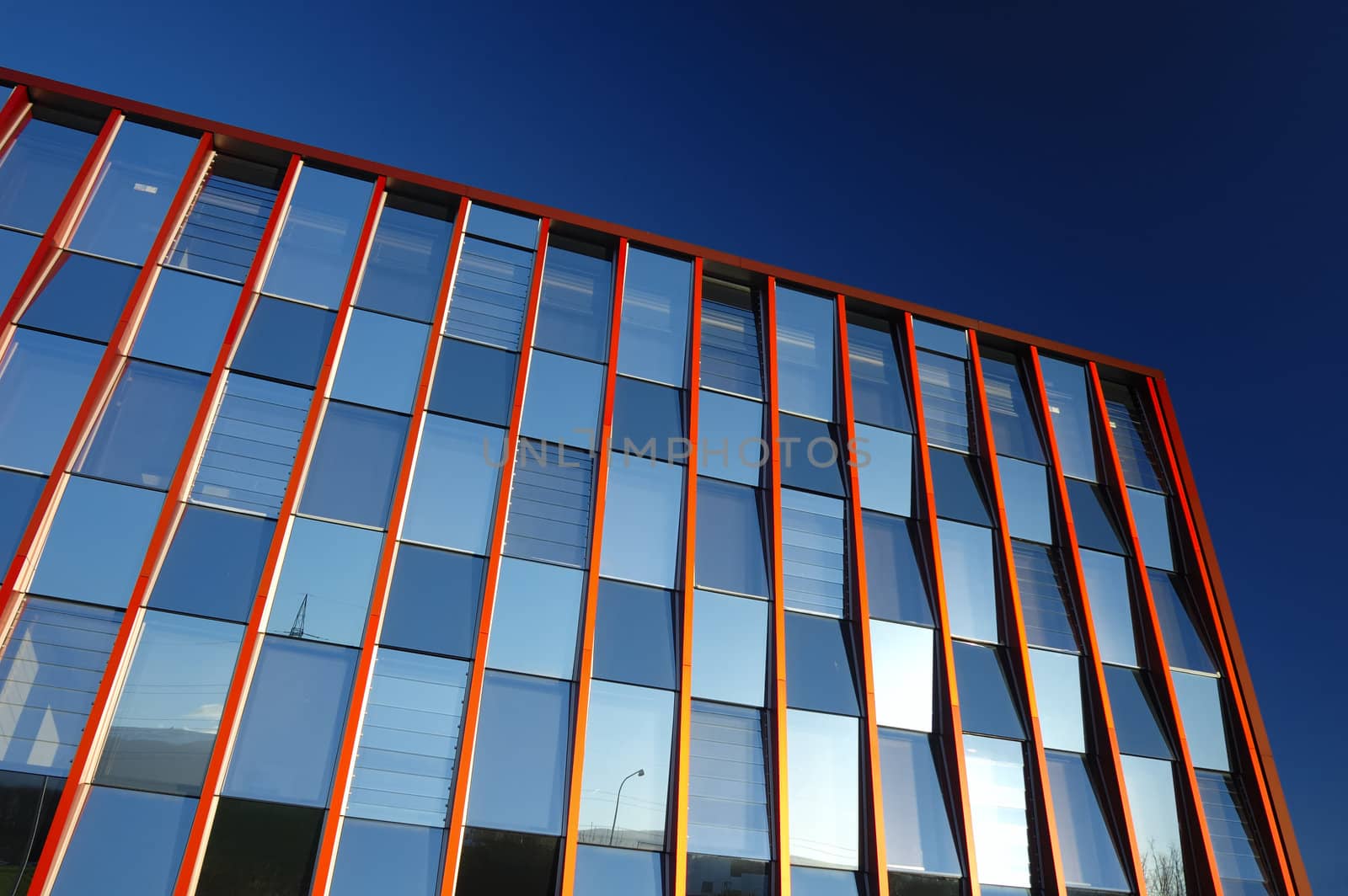 A glass-fronted office block, with little bits of the world reflected in the windows, against a clear blue sky