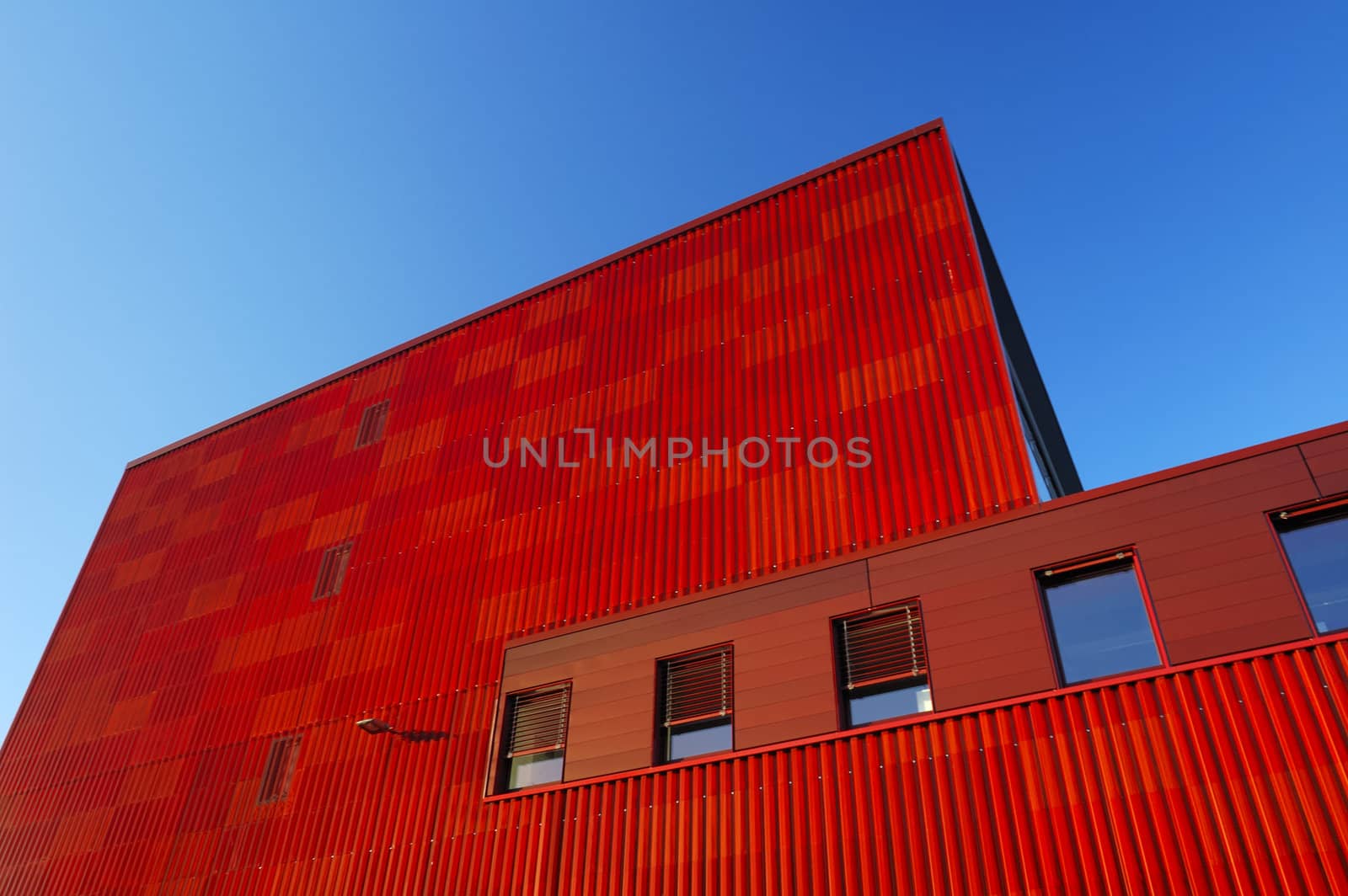 An orange factory building towers above the viewer, contrasting strongly with a clear blue sky