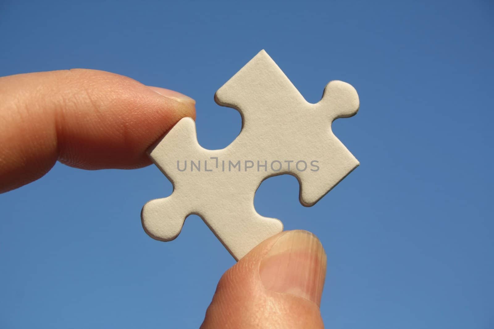 One white jigsaw puzzle piece in human fingers on a blue sky background