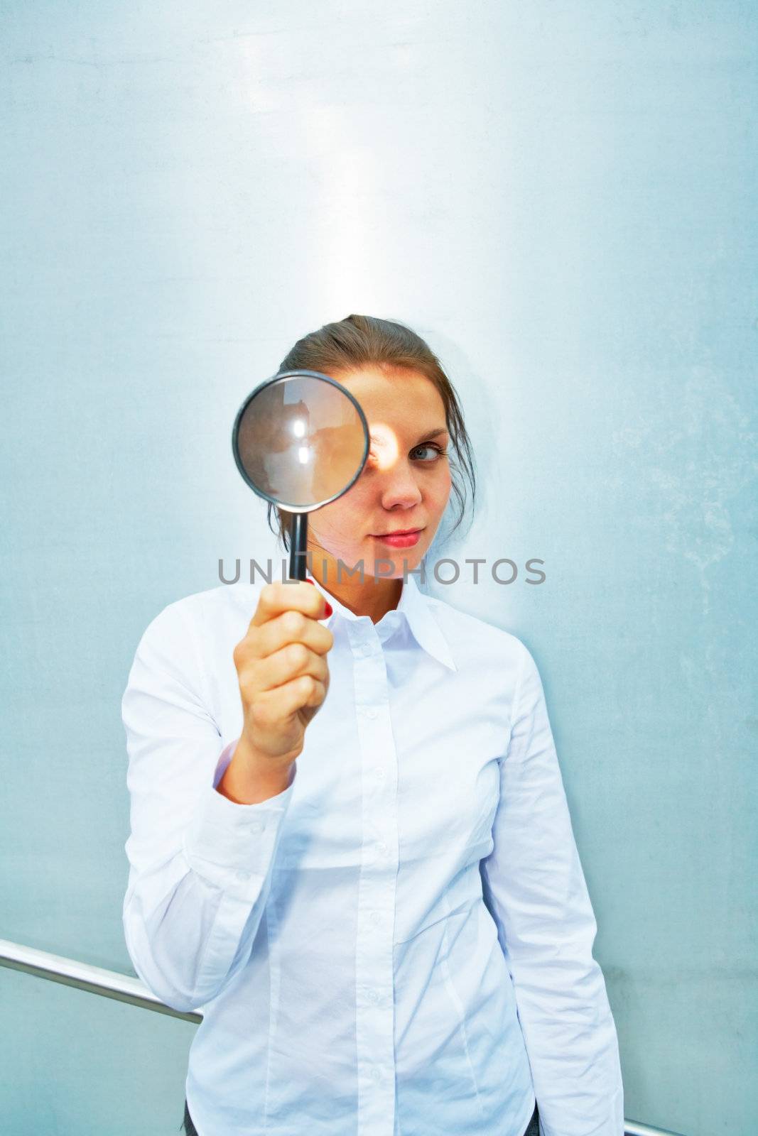 Young woman holding magnifying glass outside building