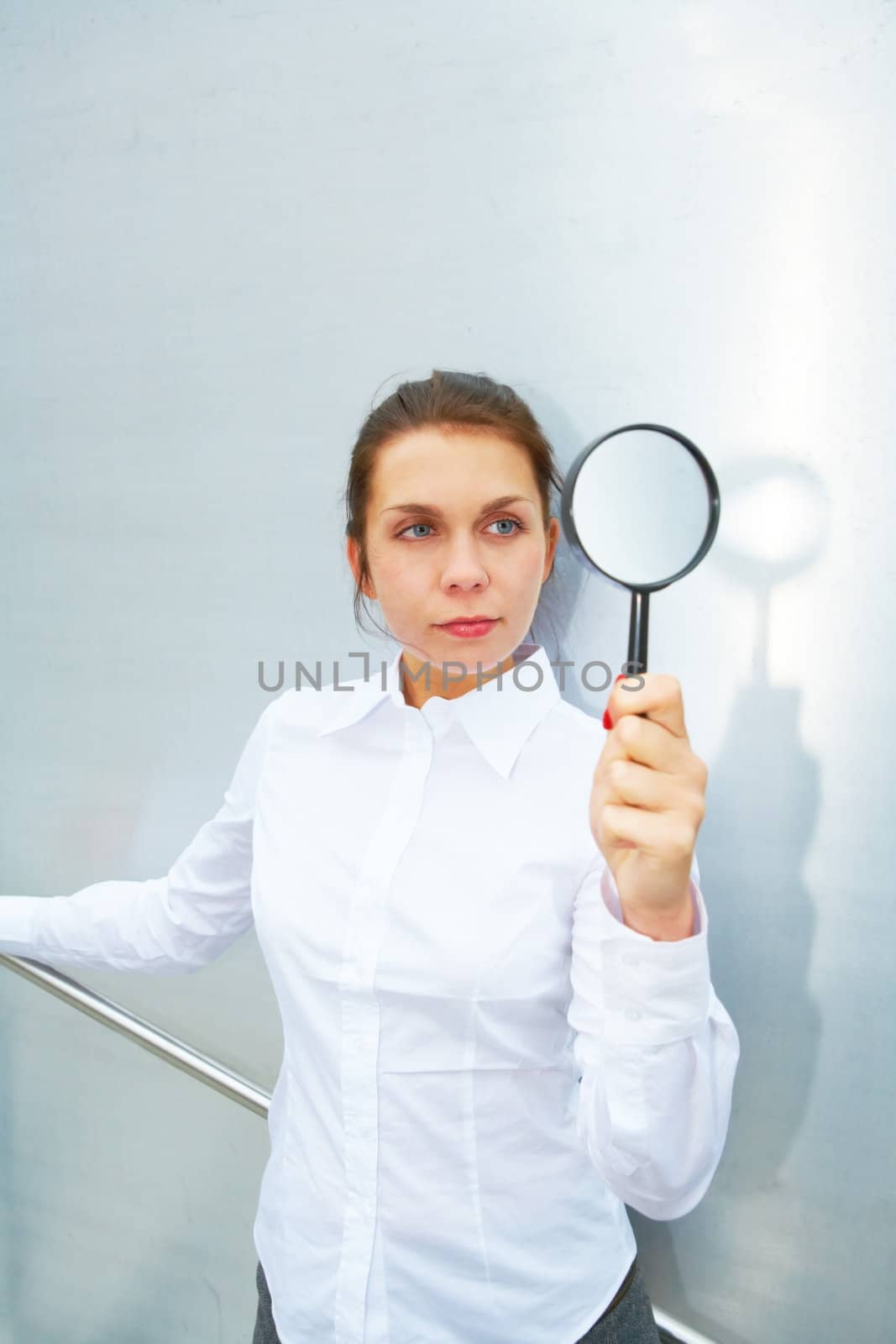 Young woman holding magnifying beside metal wall