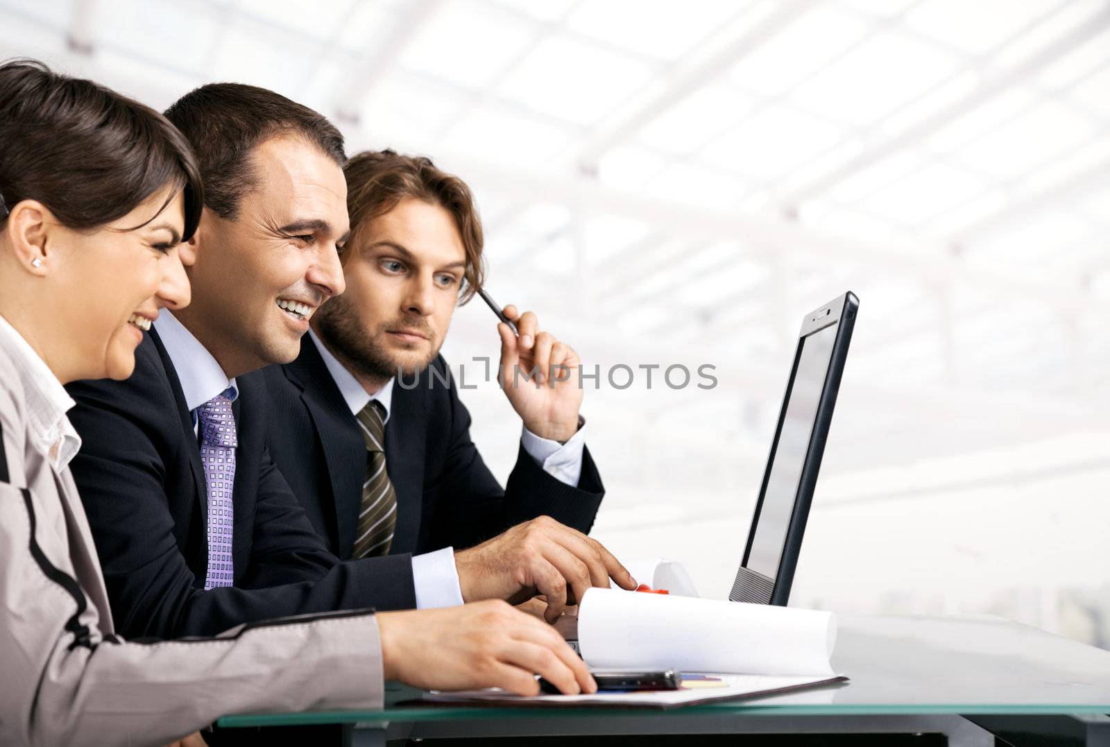 Team of three businesspeople sitting behind laptop, looking at the laptop, copyspace