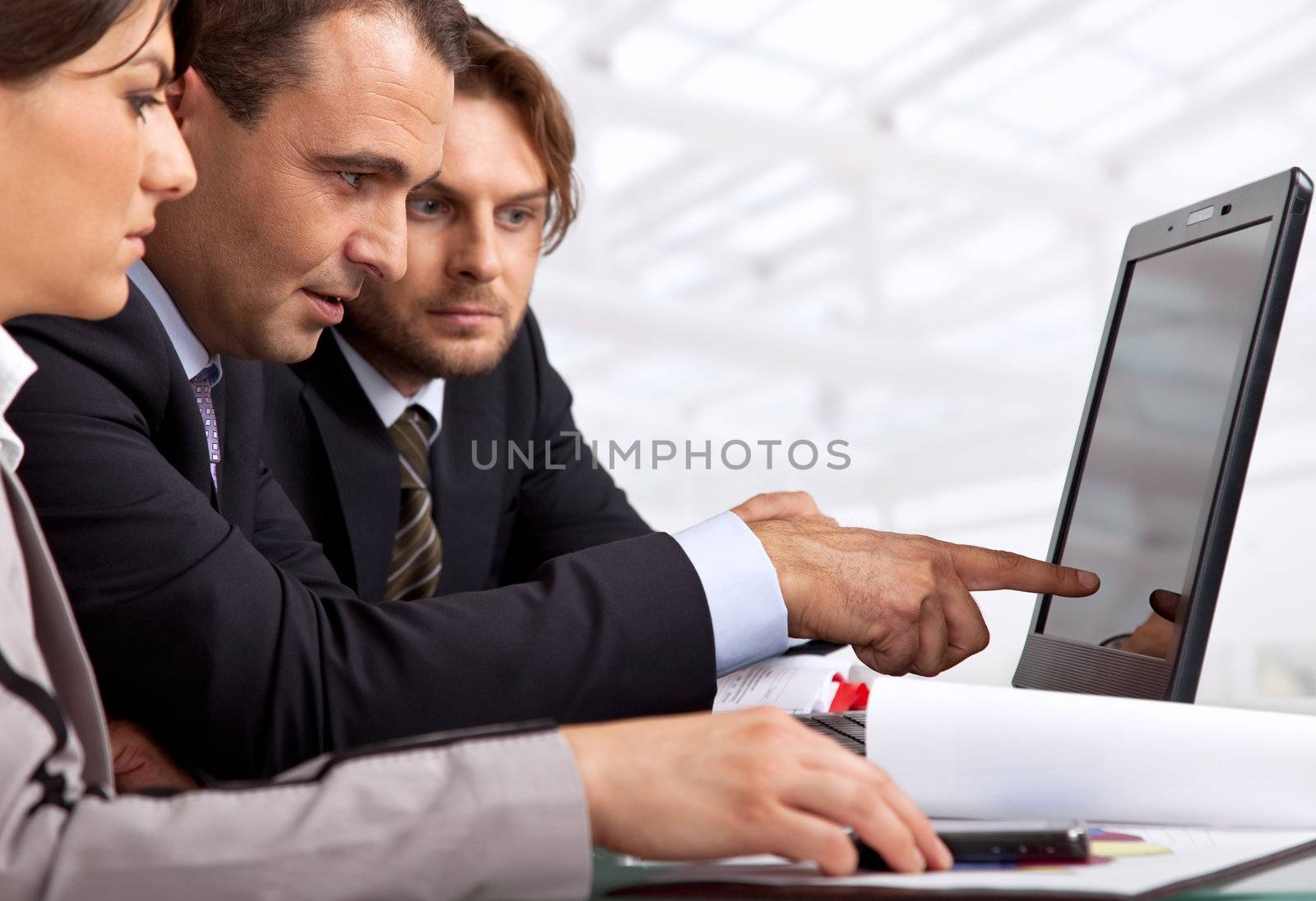 three businesspeople sitting by a laptop male is pointing at it