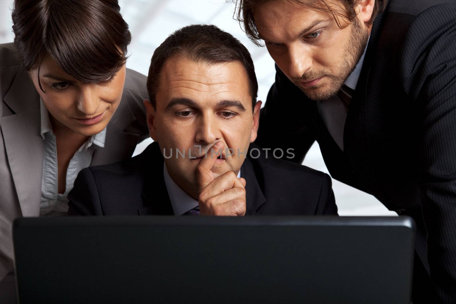 three serious business people over a laptop thinking
