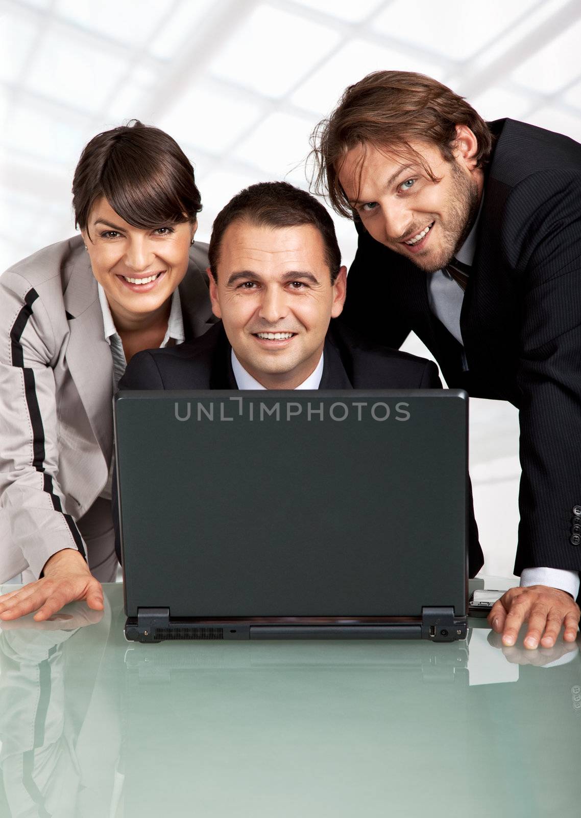 three happy business people behind a laptop, looking at camera