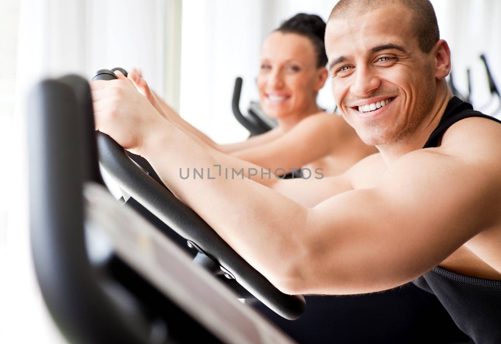 Athletic couple working out at the gym, male on focus
