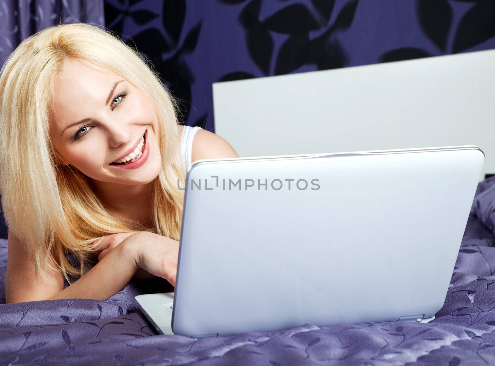 Smilingl woman using laptop on a bed, looking at camera