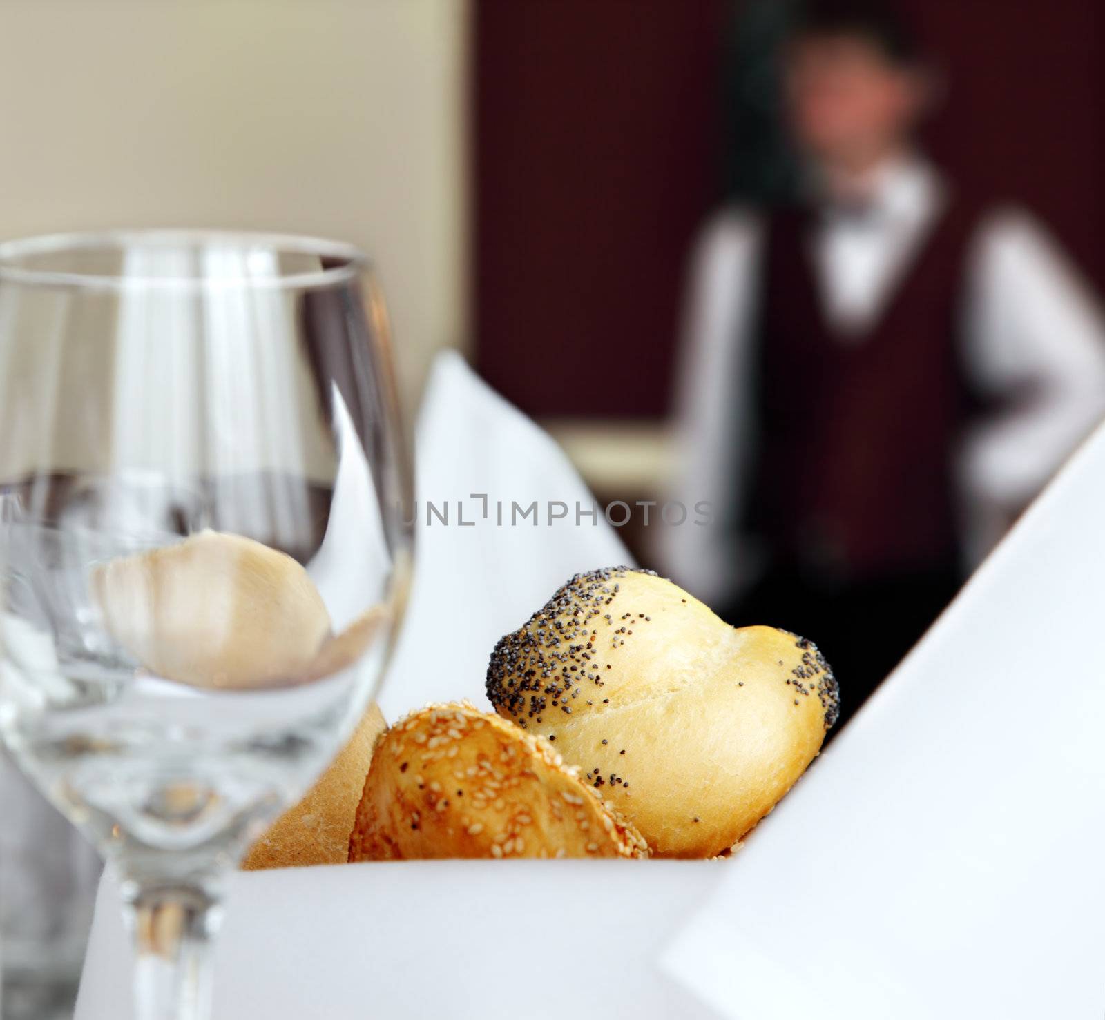 table setting in restaurant with bread empty glass and waiter off focus