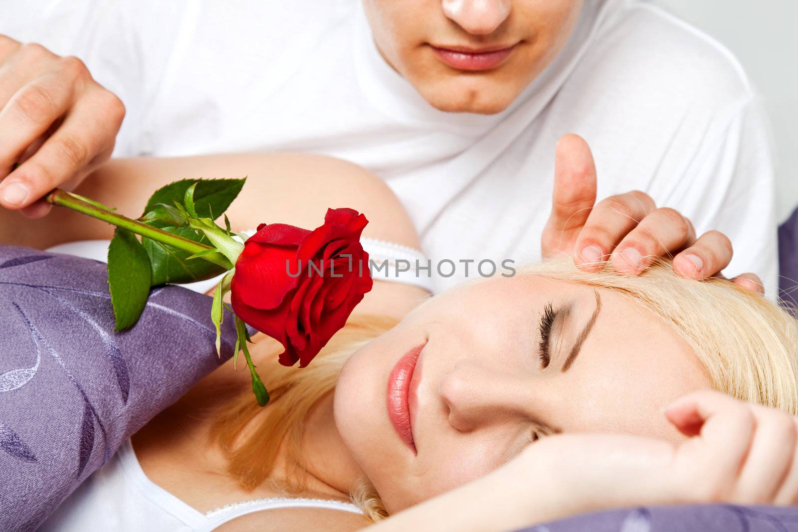 young couple in bed, male is waking female with rose