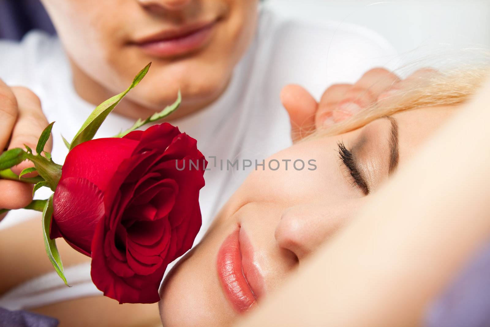 young male romantically waking up a beautiful sleeping woman with rose