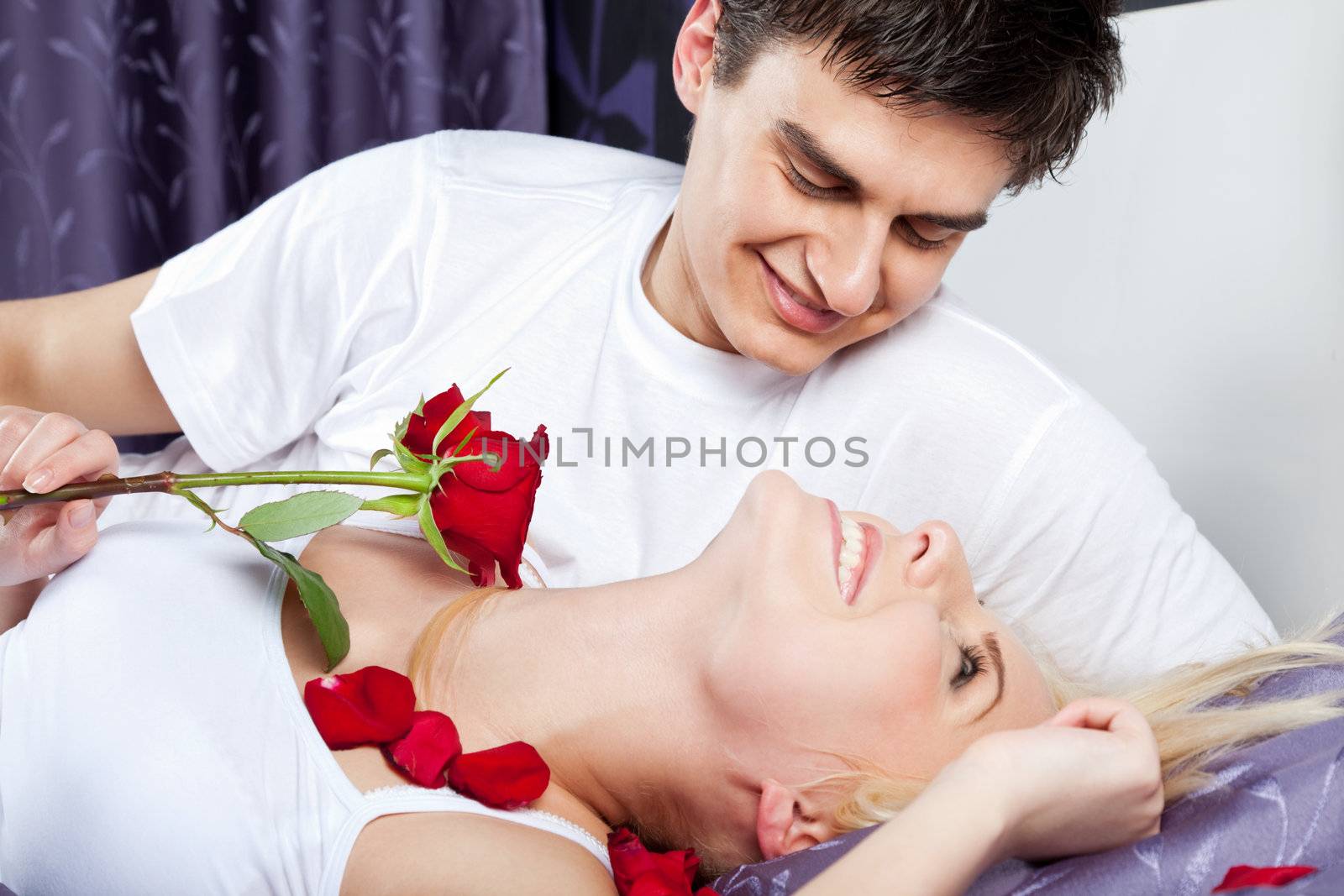 Happy young couple in bed, woman holding a red rose and smiling