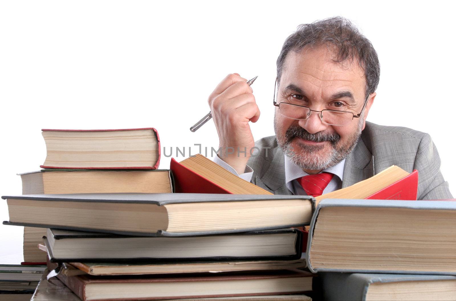 Single male is sitting behind a pile of books. Looking at camera, smiling. Holding a pen in his hand