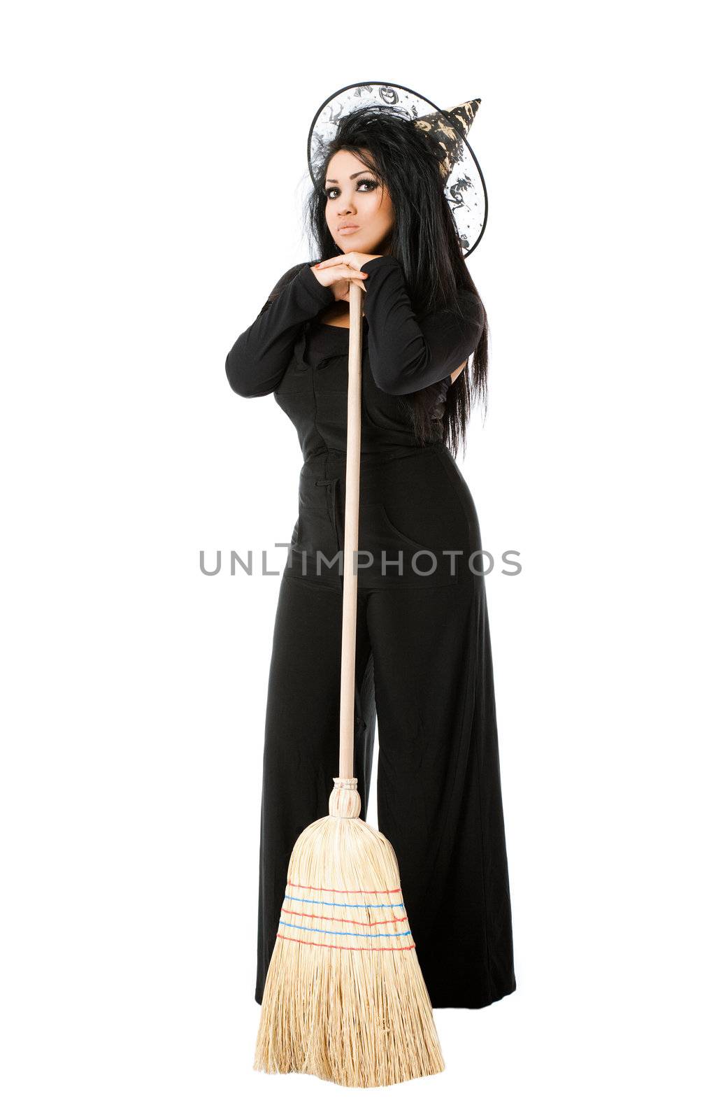 Young female with witch costume standing on white background, leaning on broom