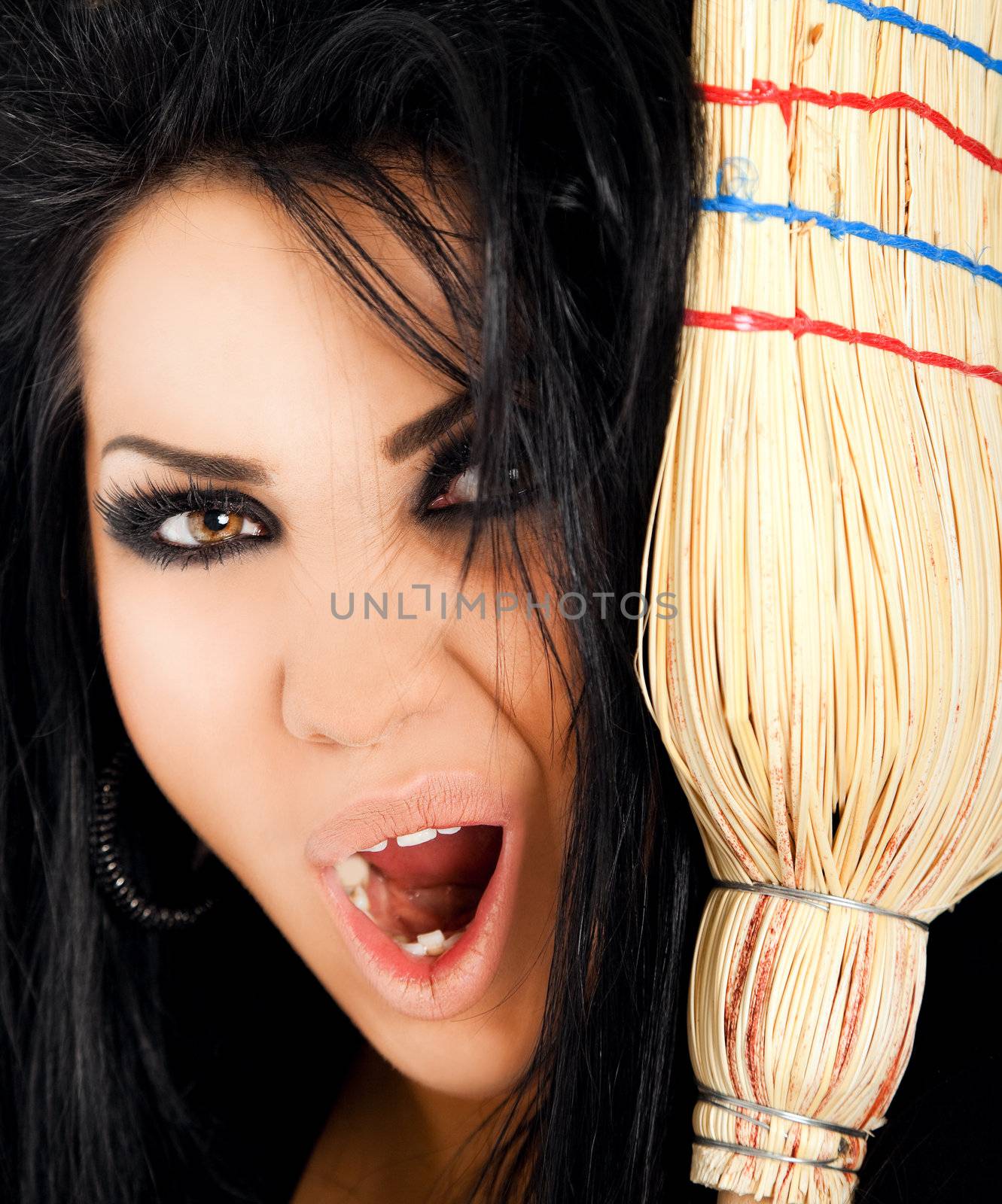 Close-up of female witch looking scary and screaming at camera behind broom