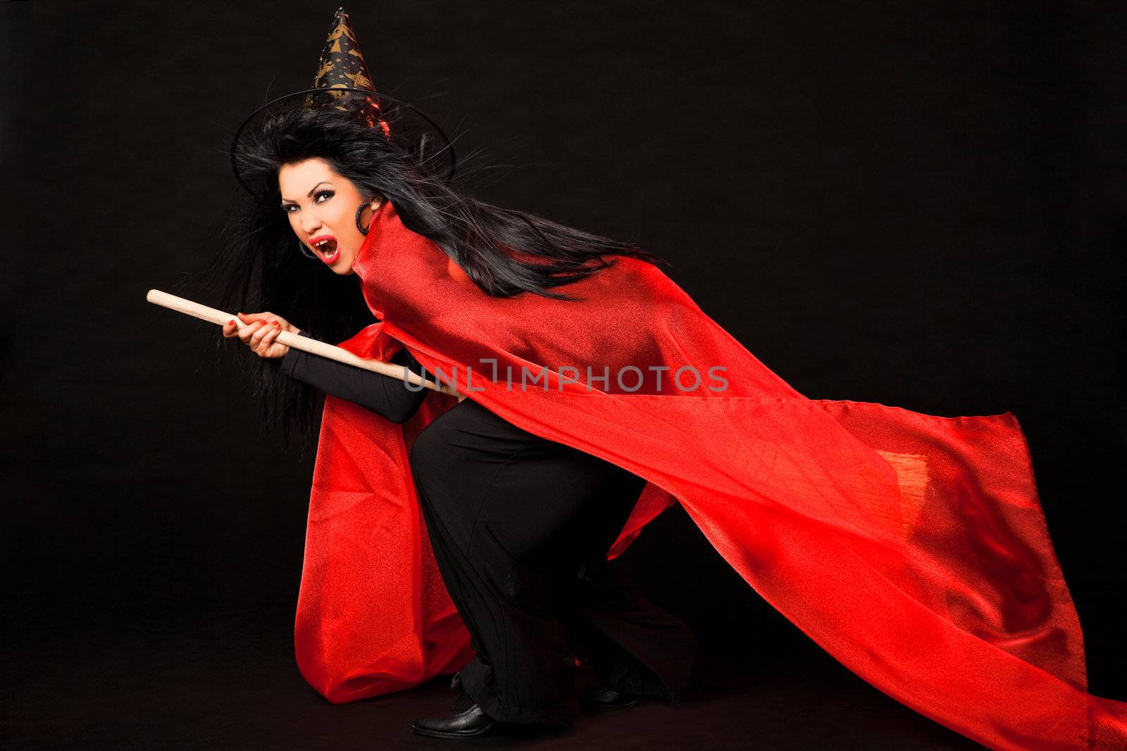 Female in witch costume with red cloak and broom between her legs screaming