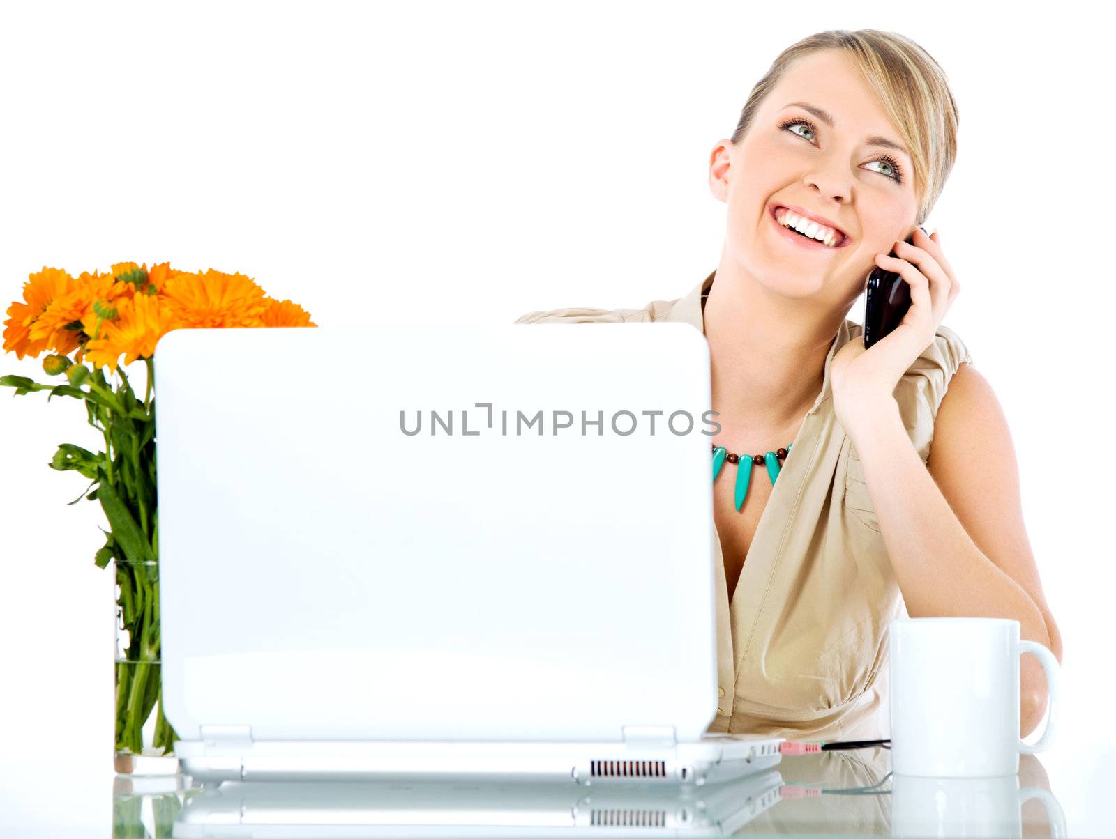 Beautiful happy female sitting behind desk with laptop, talking on the phone