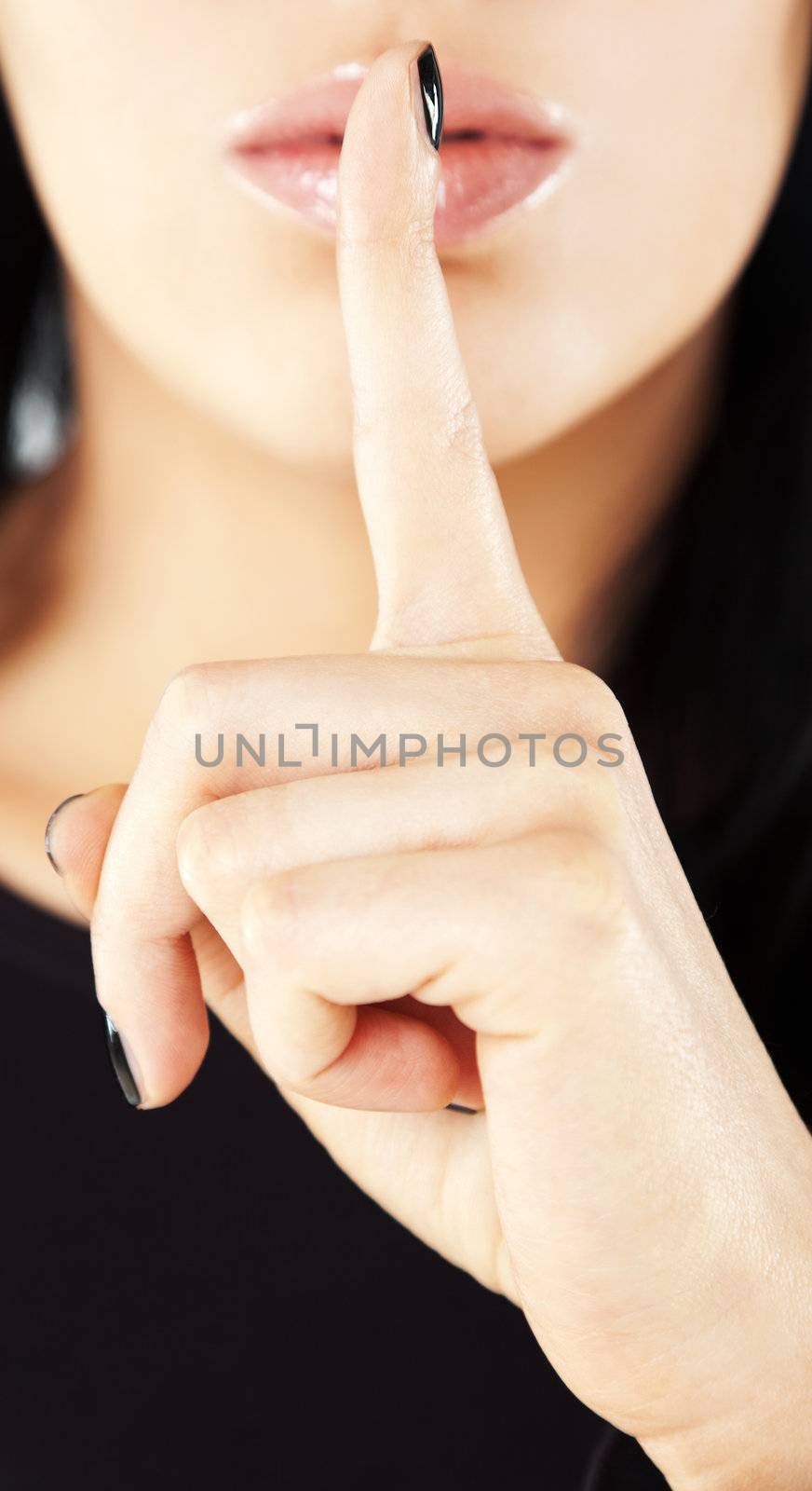Close-up of female hand, index finger on her mouth gesturing silence
