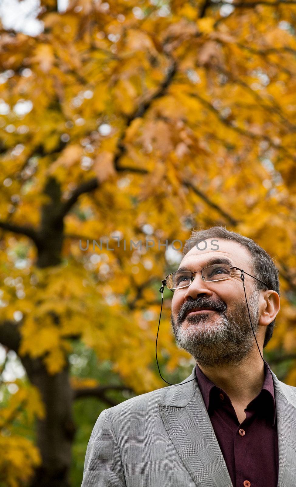 Portrait of happy adult man in autumn park, smiling and looking up