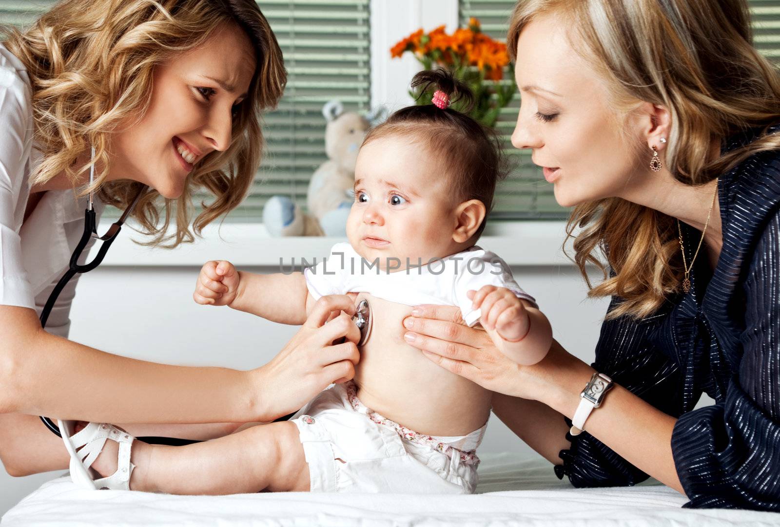 Female doctor examining with stethoscope little scared baby girl being held by mother