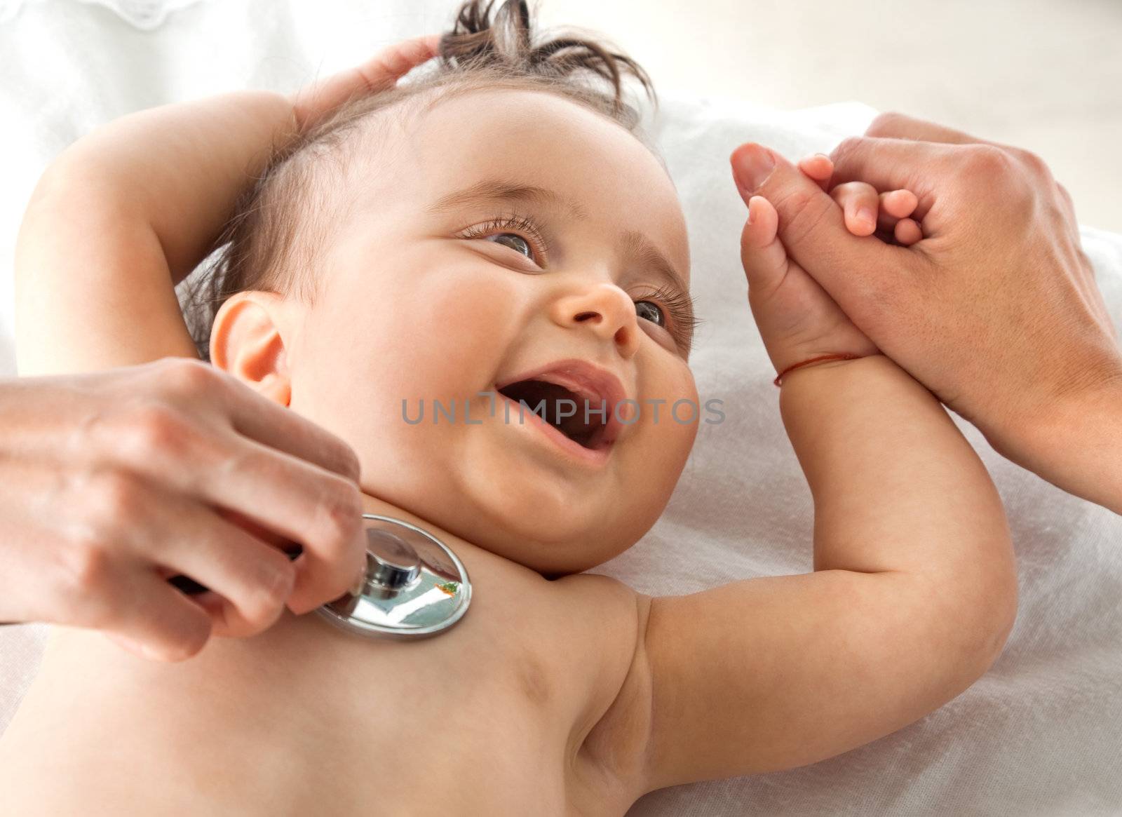 Sweet baby examined with stethoscope, holding mother's hand smiling
