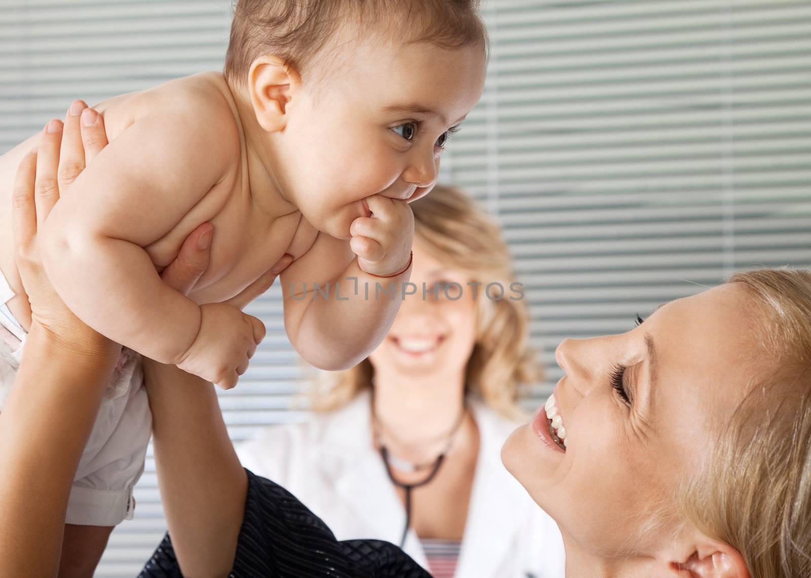 Adorable little baby girl lifted by her mother infront of smiling female doctor
