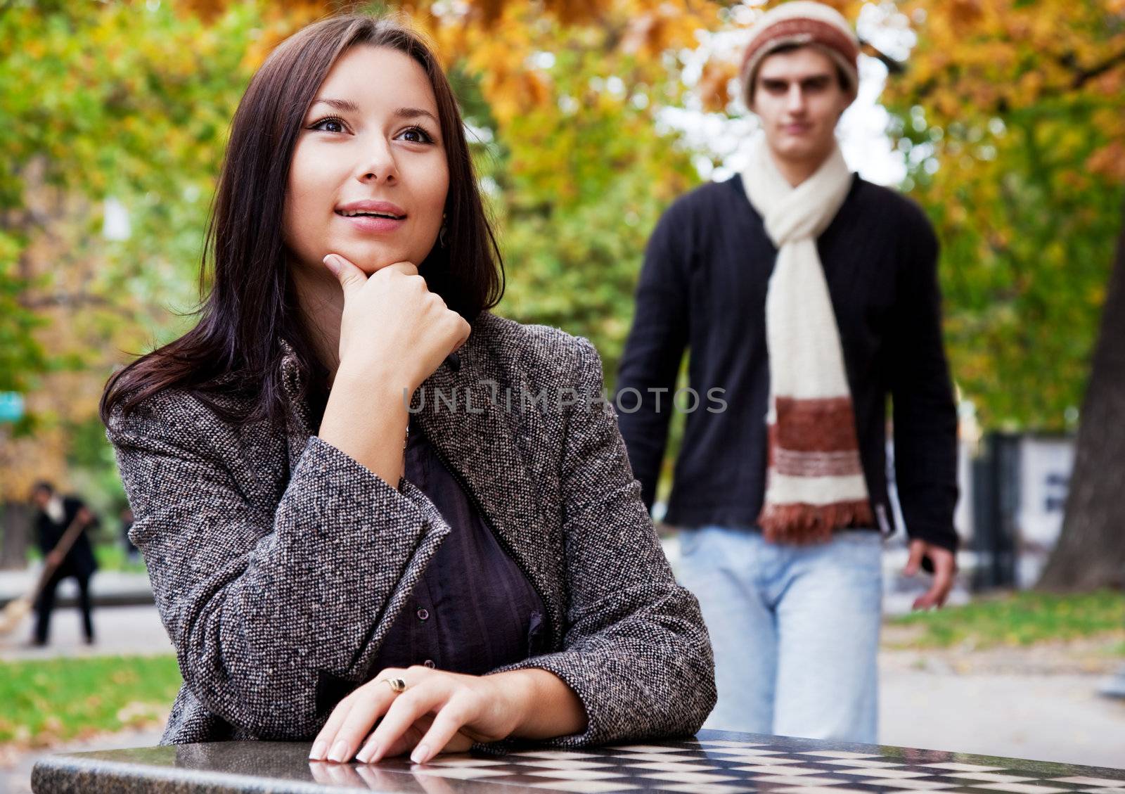 Young woman sitting in park, male coming from behind